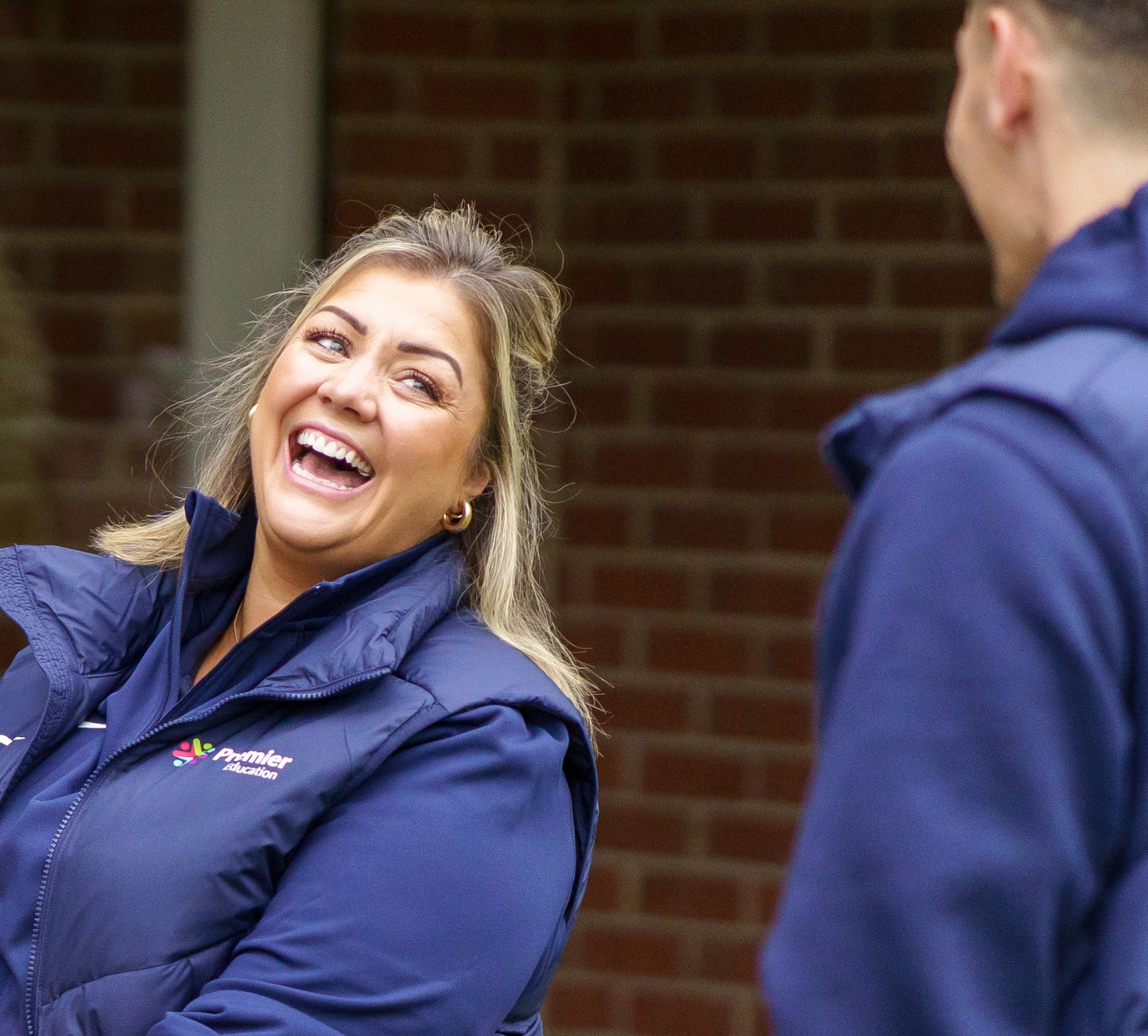 A woman in Premier Education kit laughing.