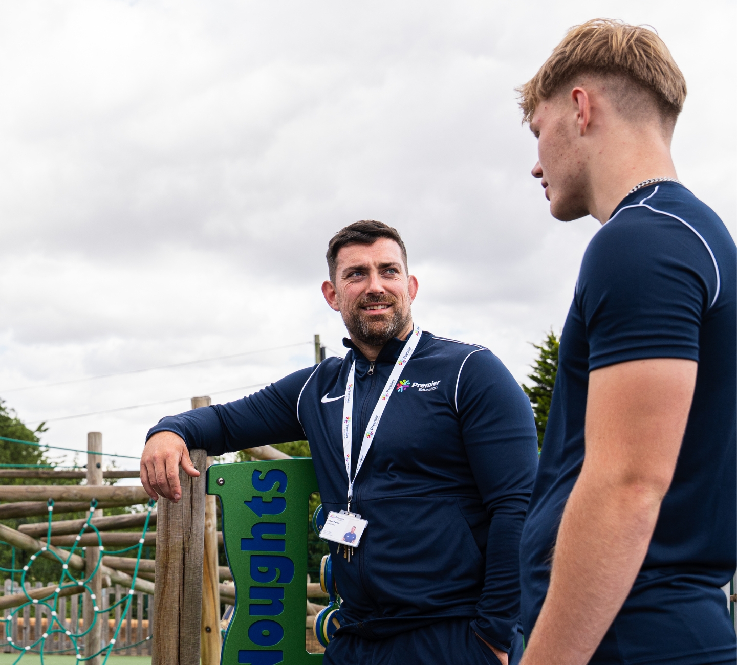 A Premier Education franchisee talks with a coach in a primary school play area.